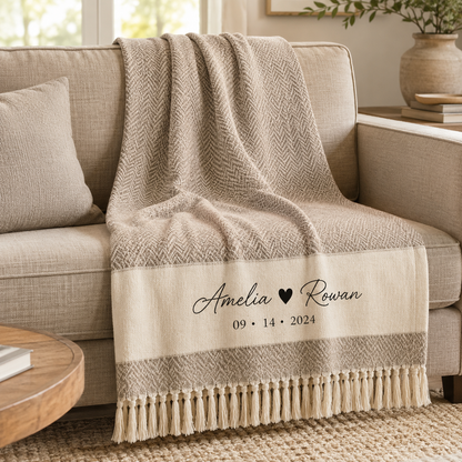 Personalized couple names and date woven throw blanket in greige herringbone style draped over a beige sofa